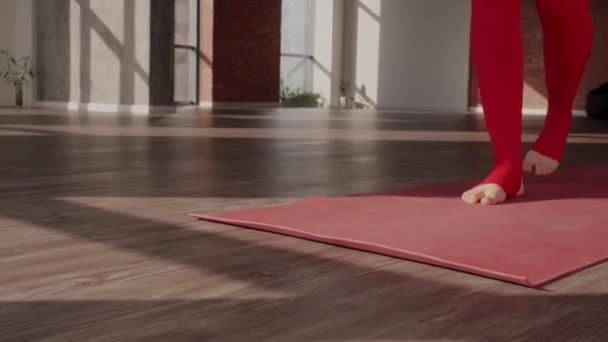 Vrouw in rood sportuniform ontvouwt sportmat en beoefent yoga in de studio. Gezonde levensstijl — Stockvideo