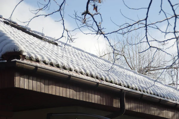 Snow on the roof in the sunshine. A winter layer cover of white down cover roofing tiles by the sun. Beautiful seasonal rural view.