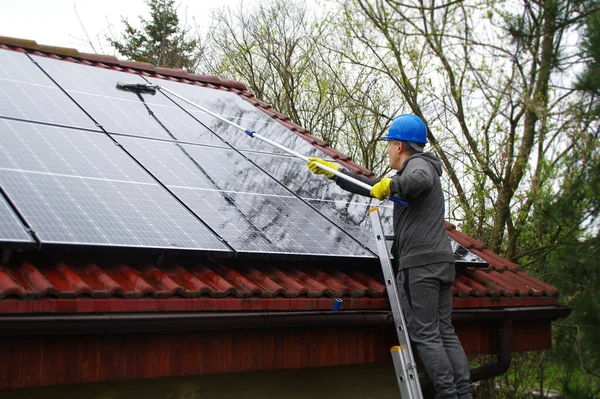 Güneş panellerini temizliyorum. Merdivendeki bir adam fotovoltaik bir tesisi temizleyip yıkıyor..