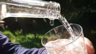 Yavaş çekimde şişeden bardağa temiz su dökmek. Susuzluk giderme ve içecek konsepti.