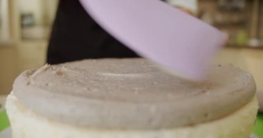 Yakın plan. Elinde metal spatulayla pastaya tereyağı kremi süren bir kadın. V2