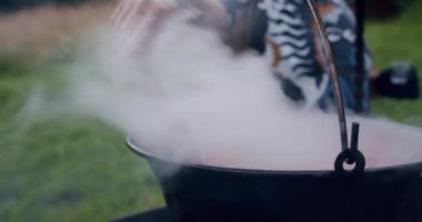 Büyük bir kaşık dolusu mantar çorbası açık ateşte büyük bir kazanda pişirilir. Yavaş çekim V3