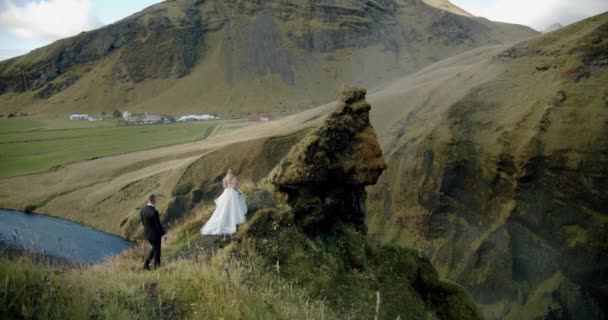 Casal de casamento, o noivo vem à noiva no fundo de uma cachoeira. Islândia Wide shot — Vídeo de Stock