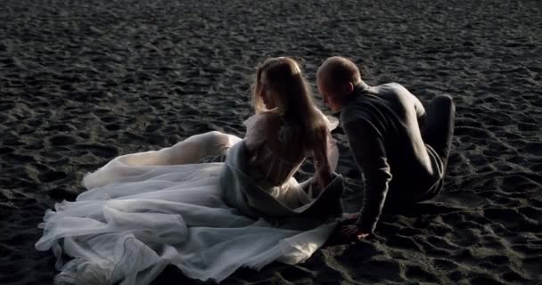Αγαπημένο ζευγάρι κάθεται μαζί στη μαύρη άμμο και κρατώντας τα χέρια, ηλιόλουστη μέρα ανέμου. Ισλανδία Αργή κίνηση — Αρχείο Βίντεο