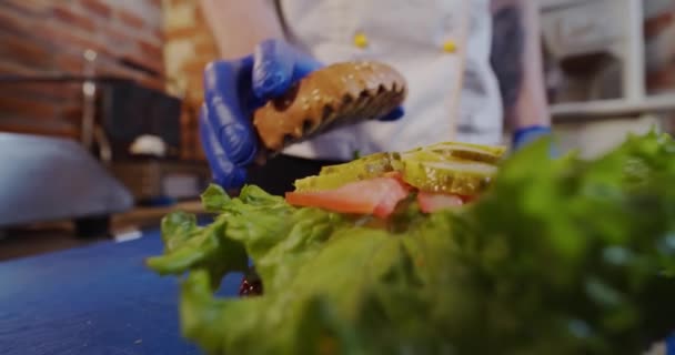 Der Koch reicht einem Burger ein Top-Brötchen. Aus nächster Nähe. Zeitlupe — Stockvideo