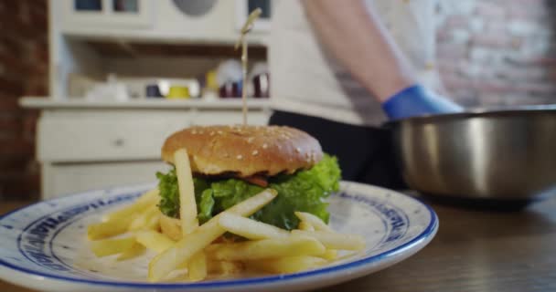 Chef puts french fries on a plate with a large burger. slow motion. — Stock Video