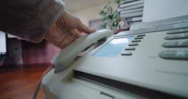 Kapatın. Faks çeken bir kadının eli düğmeye basar ve telefonu açar.,