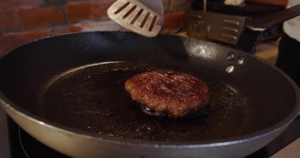 El cocinero prepara una hamburguesa, retira la chuleta de la sartén y la pone en la hamburguesa. De cerca. Movimiento lento — Vídeo de stock