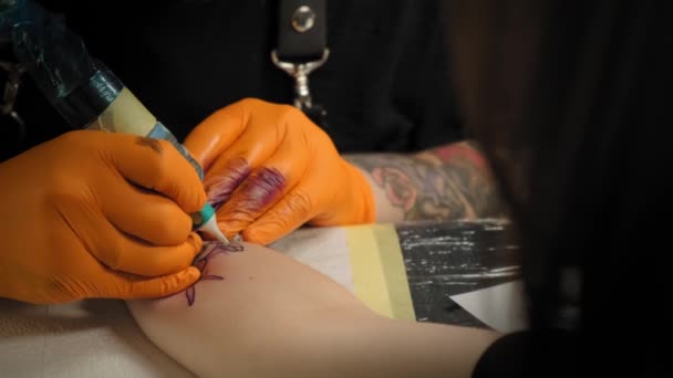 Tatuaje artista dibuja un cuadro en la mano de una mujer joven, el proceso de creación de un tatuajecon luz azul. Cámara lenta Vista de cerca — Vídeo de stock