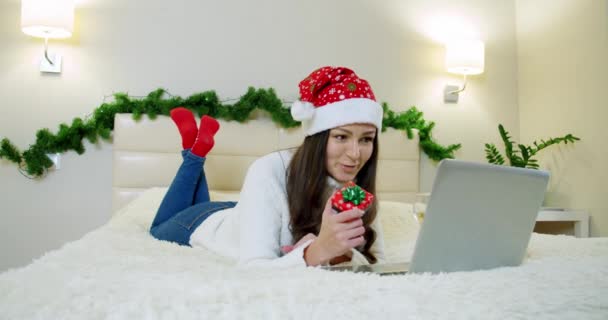 Vakantie kerstmis interieur winter concept. jonge vrouw in gezellige slaapkamer met laptop liggen op bed thuis. — Stockvideo