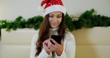 Kapatın genç ve güzel bayan kanepeye oturun ve akıllı telefon kullanın, noel festivali.