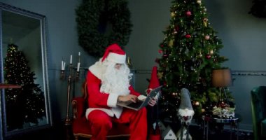 Noel Baba kostümlü adam oturma odasında oturmuş bilgisayarın başında görüntülü sohbet ediyor..