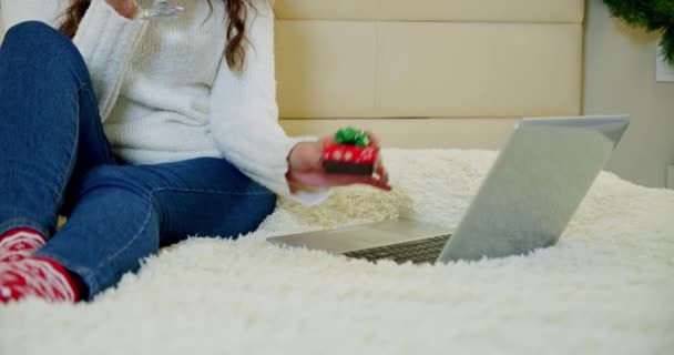 Gros plan cadeau. Vacances Noël intérieur concept d'hiver. jeune femme dans une chambre confortable avec ordinateur portable couché sur le lit à la maison et tenant un cadeau dans sa main. — Video