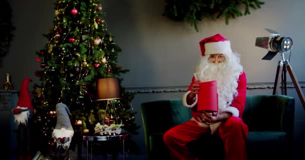 Close up portret Papai Noel abre caixa de presente brilhante mágico e olha para dentro, a luz brilhante brilha da caixa. Movimento lento Wide shot — Vídeo de Stock