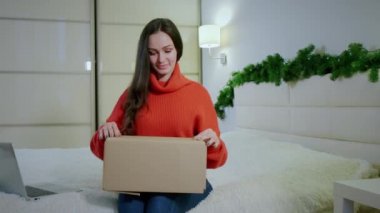 Mutlu genç tüketici kız elinde karton kutu tutarak evdeki kanepede oturuyor..