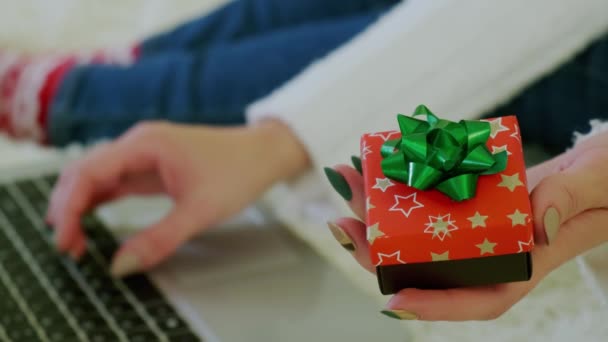 Hediyeyi kapat. Tatil Noel kış konsepti. Evde dizüstü bilgisayarı olan ve elinde kırmızı bir hediye tutan genç bir kadın.. — Stok video