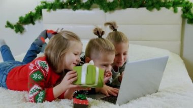 Yılbaşı konsepti, çocuklar Noel kıyafetleriyle kanepede yatar ve bir dizüstü bilgisayarla internetten arama yaparlar..