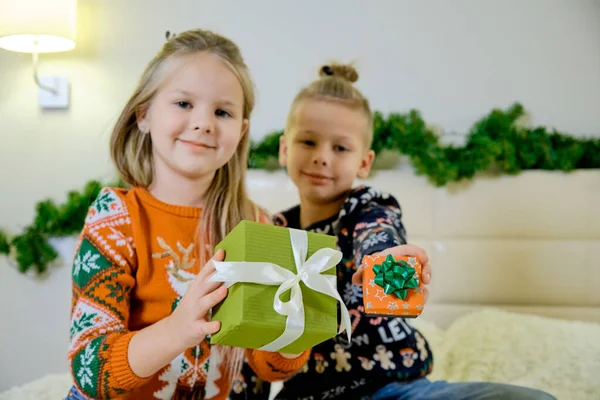 Koncepcja sylwestrowa, dzieci leżą na kanapie w świątecznych ciuchach i trzymają prezenty w rękach. — Zdjęcie stockowe
