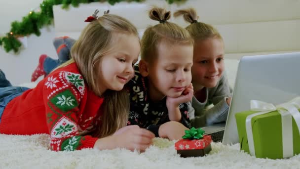 Concepto de Año Nuevo, los niños yacen en el sofá con ropa de Navidad, y hacer una llamada en línea en un ordenador portátil. De cerca. — Vídeo de stock