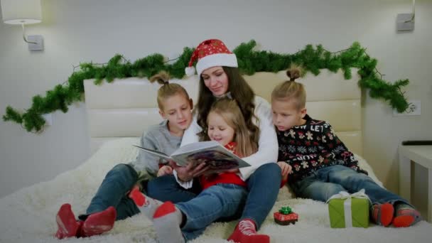 En la atmósfera de Año Nuevo, la madre lee un libro a su familia. — Vídeo de stock