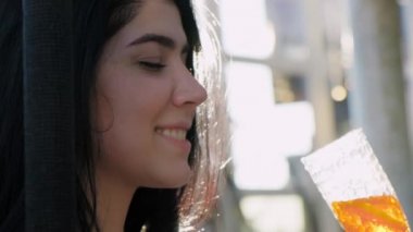 Portret. Havuzun kenarında sallanan sandalyede elinde güneş ışığında kokteyl olan güzel bir kız. Yavaş çekim