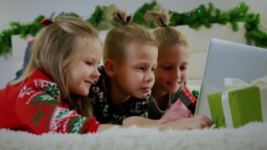 Yeni yıl konsepti, çocuklar Noel kıyafetleriyle kanepede yatar ve bir dizüstü bilgisayarla online arama yaparlar. Kapatın çocuklar.