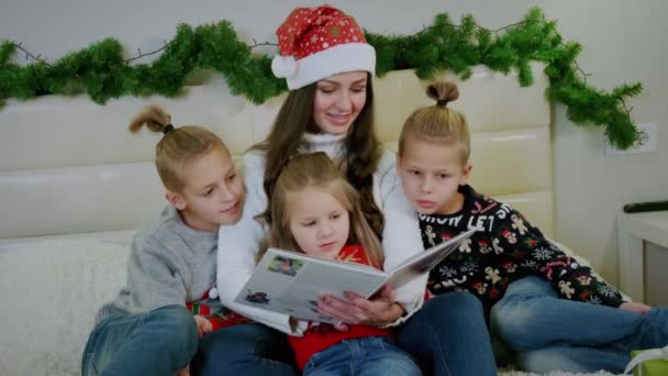 Na atmosfera de Ano Novo, a mãe lê um livro para sua família. Tiro largo — Vídeo de Stock