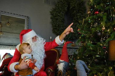 Sevimli küçük çocuk ve Noel Baba hediye kutusunu tutuyorlar ve Noel ağacına bakıyorlar..