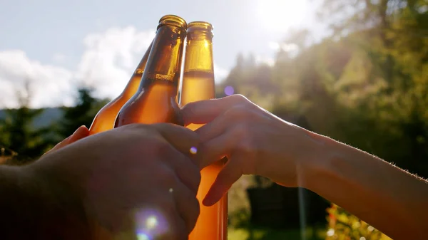 Celebration beer cheers concept, hands holding up bottles of beer of people group in outdoor party vacation in mountain. Close up.