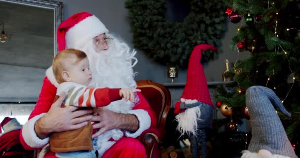 Милый маленький мальчик и Санта Клаус держат коробку подарков и посмотрите на рождественскую елку. Закрыть — стоковое видео