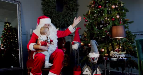 Roztomilý malý chlapec a Santa Claus drží dárkové krabice a podívejte se na vánoční stromeček. — Stock video