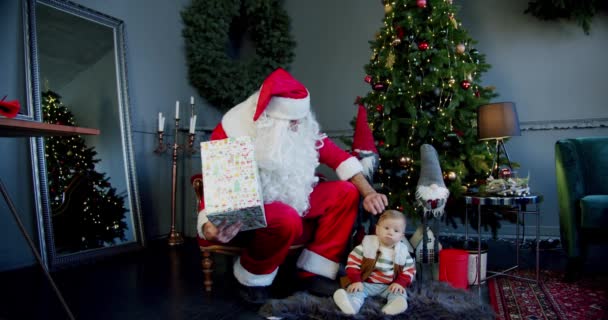 เด็กน้อยน่ารักและซานตาคลอสถือกล่องของขวัญและมองไปที่มัน แนวคิดปีใหม่ — วีดีโอสต็อก