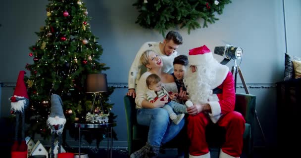 Rodina spolu se Santa Clausem sedí na pohovce a podlahách a dívá se do kamery. — Stock video