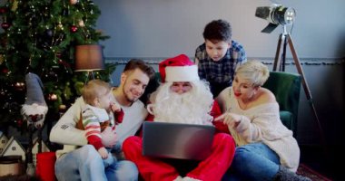 Mutlu bir aile, Noel Baba 'yla birlikte kanepede oturup dizüstü bilgisayara bakıyorlar. Yakın çekim.
