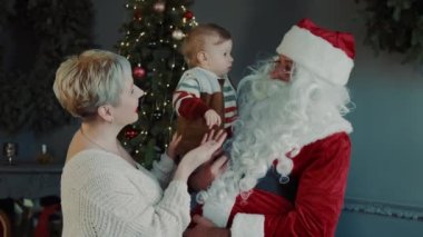 Annesinin kollarında güzel bir bebek ve Noel Baba birbirlerine bakıyorlar..