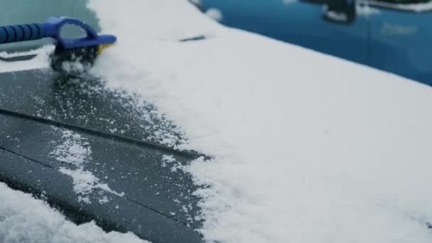 Kvinnliga händer rengör snöbilen med en pensel. Snöfall täckte bilen. Långsamma rörelser — Stockvideo