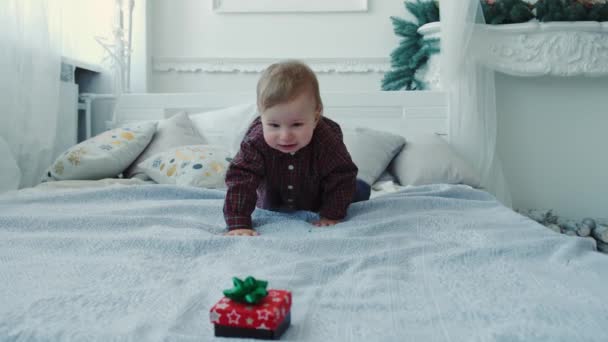 Slow motion en liten pojke kryper på sängen för en gåva och försöker äta den. V2 — Stockvideo