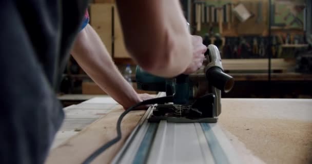 Медленное движение. Мастер режет деревянную доску циркулярной пилой в деревообрабатывающей мастерской небольшого производителя мебели. — стоковое видео
