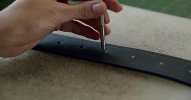 Zbliżenie ujęcia specjalisty pracującego ze skórą, kobiece dłonie rzemieślniczki robią dziury w skórzanym pasku — Wideo stockowe
