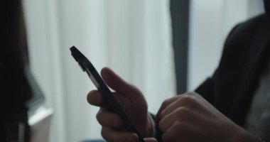 Siyah takım elbiseli bir iş adamı akıllı telefonunu kullanıyor ve konuşuyor.