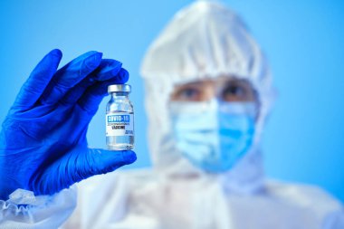 Mavi doktor ya da hemşire kişisel koruyucu ekipman takıyor ve laboratuarda ya da hastanede Corona covid-19 aşısı taşıyor.