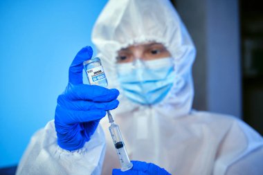 Mavili doktor ya da hemşire kişisel koruyucu ekipman kullanıyor ve aşıyı ampulden laboratuarda ya da hastanede Corona covid-19 aşısı ile topluyor..