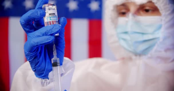 Γαλάζιος ιατρός ή νοσοκόμος που φορά μέσα ατομικής προστασίας και κρατά σύριγγα του εμβολίου κατά του ιού του κόκορα covid-19 σε εργαστήριο ή νοσοκομείο με φόντο τη σημαία του ΟΗΕ — Αρχείο Βίντεο