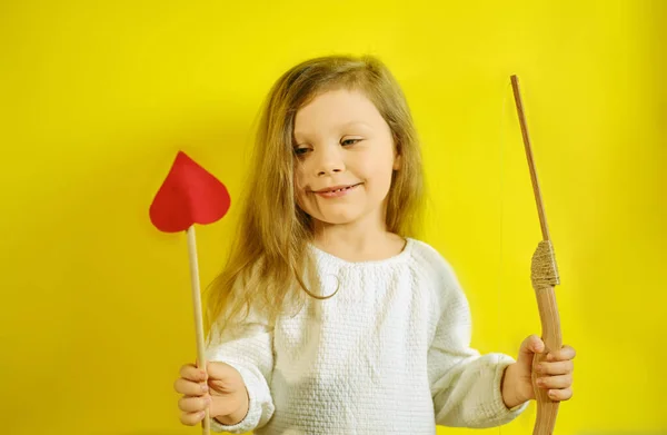 Retrato de niña sosteniendo una flecha en forma de corazón y una ballesta sobre fondo amarillo con espacio para copiar. — Foto de Stock