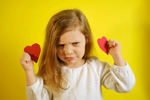 Retrato de niña molesta o insatisfecha sosteniendo un corazón rojo para usted, aislado sobre fondo amarillo con espacio para copiar. — Foto de Stock