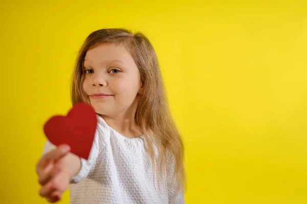 Retrato de niña sosteniendo un corazón rojo para ti, aislado sobre fondo amarillo con espacio para copiar. V3 — Foto de Stock