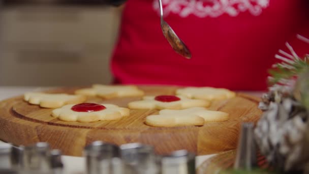 Vista de cerca de una mano de mujer haciendo una galleta de jengibre usando una cuchara, pone la mermelada en las galletas. Concepto de Navidad y Año Nuevo — Vídeo de stock