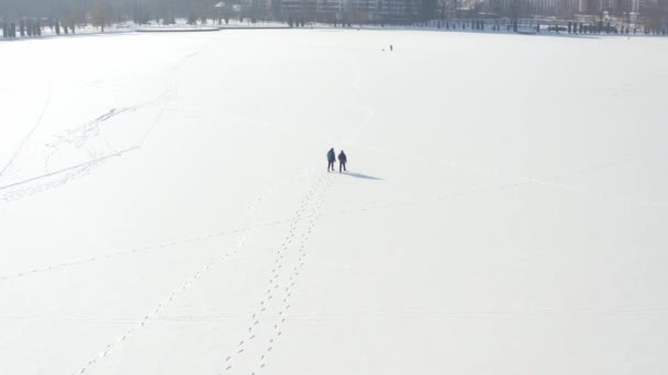 Prise de vue aérienne après deux hommes marchant sur un champ enneigé ou un lac en cas de catastrophe enneigée. — Video