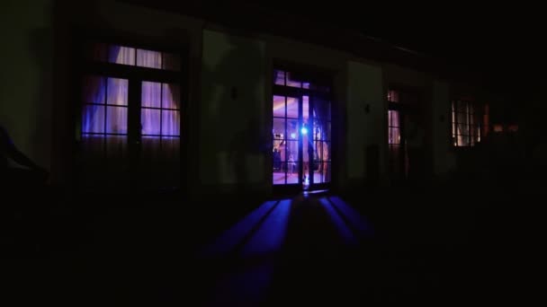 Gruppo di persone sagomate che ballano in una sala banchetti buia per un ricevimento di nozze, vista dalle finestre. — Video Stock