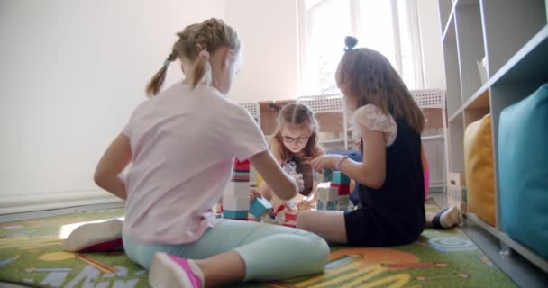 Dzieci przedszkolaki pomagające budować drewniane klocki razem siedzieć na podłodze dywan. — Wideo stockowe